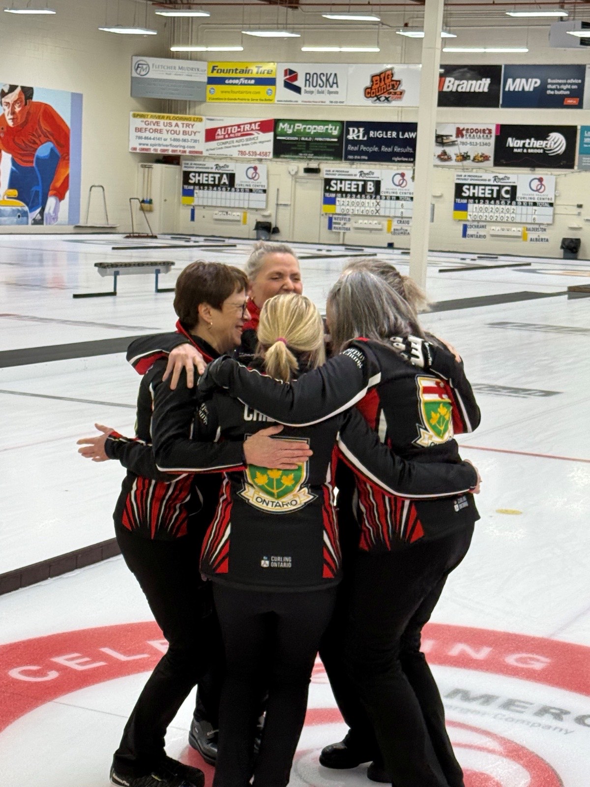 L'équipe féminine de l'Ontario célébrant dans une accolade de groupe sur la glace